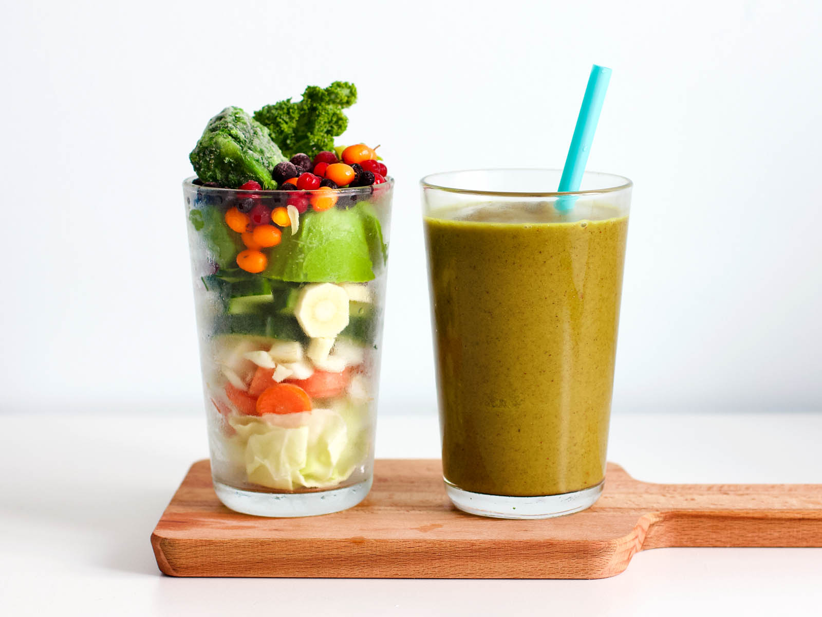 Glass with fruits and vegetables placed near another glass with freshly made green smoothie