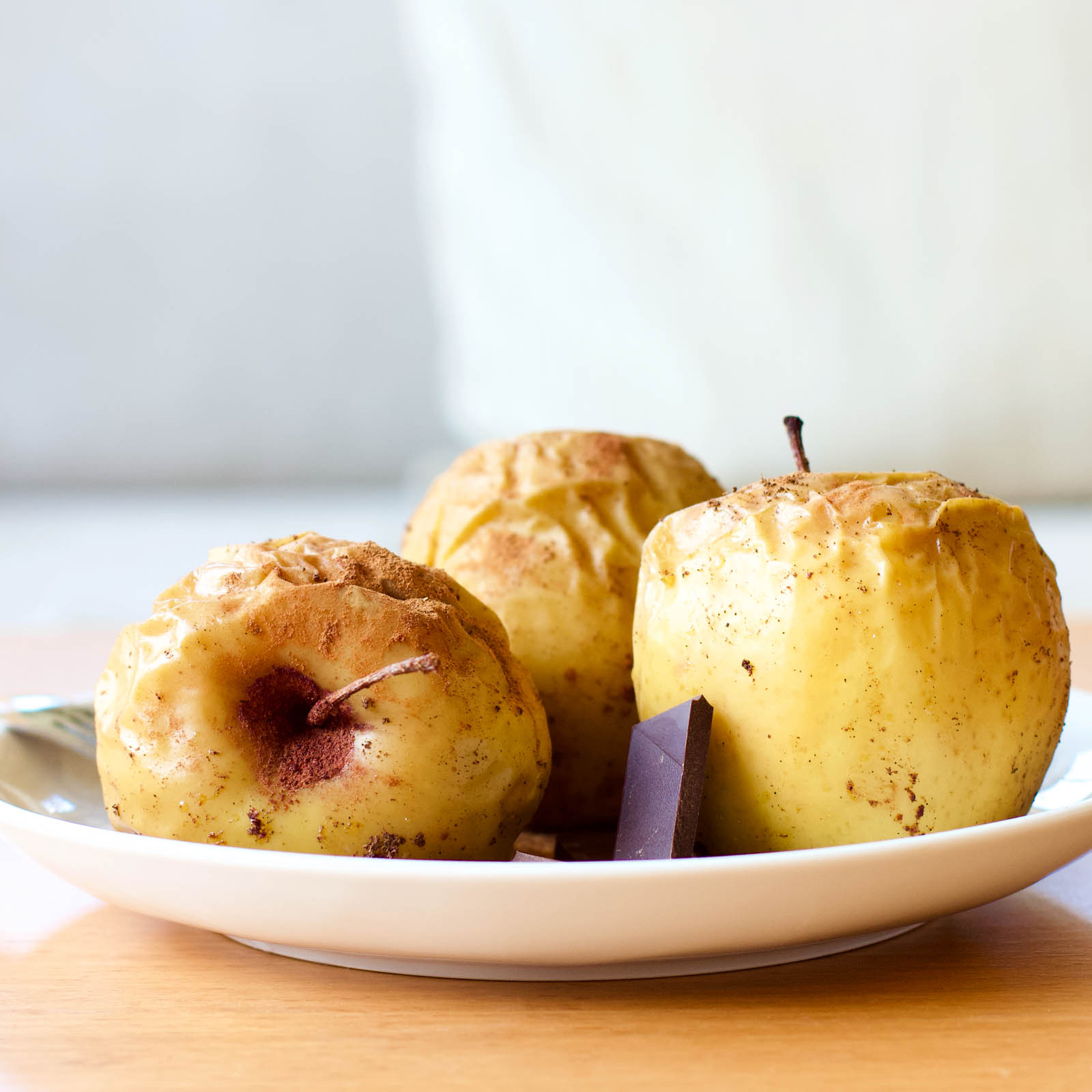 Three Cinnamon Baked Golden Apples on a plate, served with dark chocolate squares