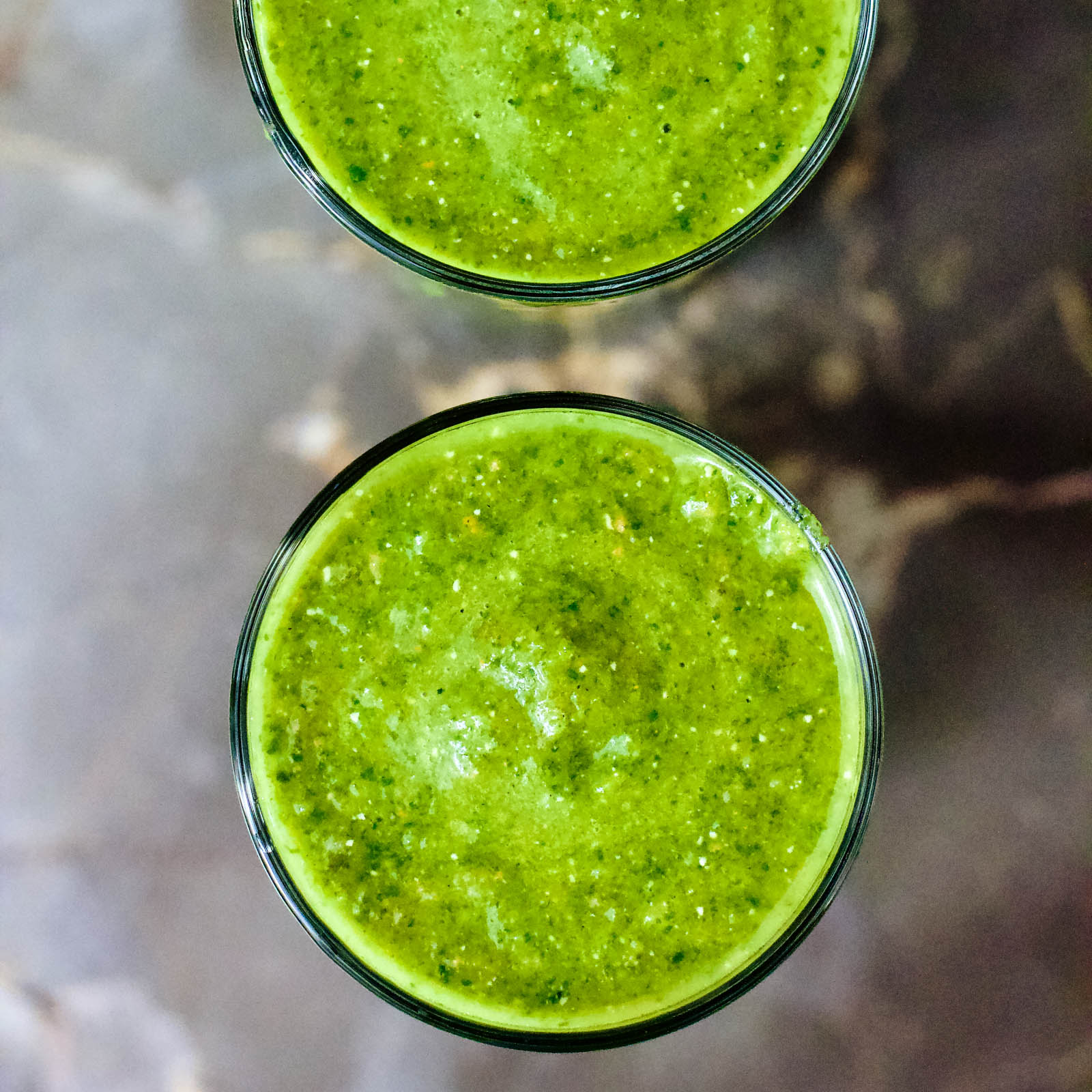 Two glasses of freshly made Spinach Pineapple Green Smoothie on a marble table, top-down view