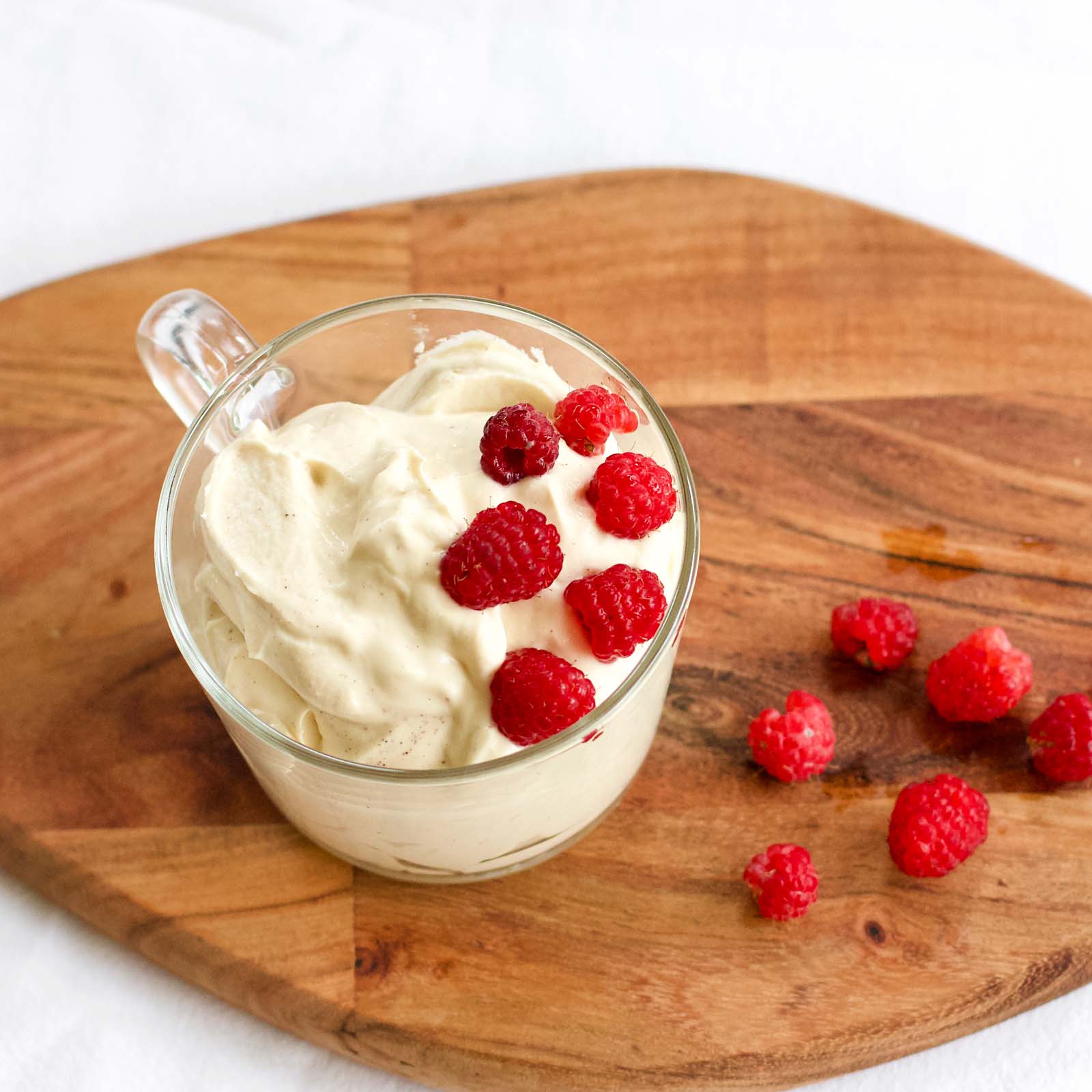 Homemade Raspberries Whipped Cream Dessert with fresh raspberries on the side, on a wooden board