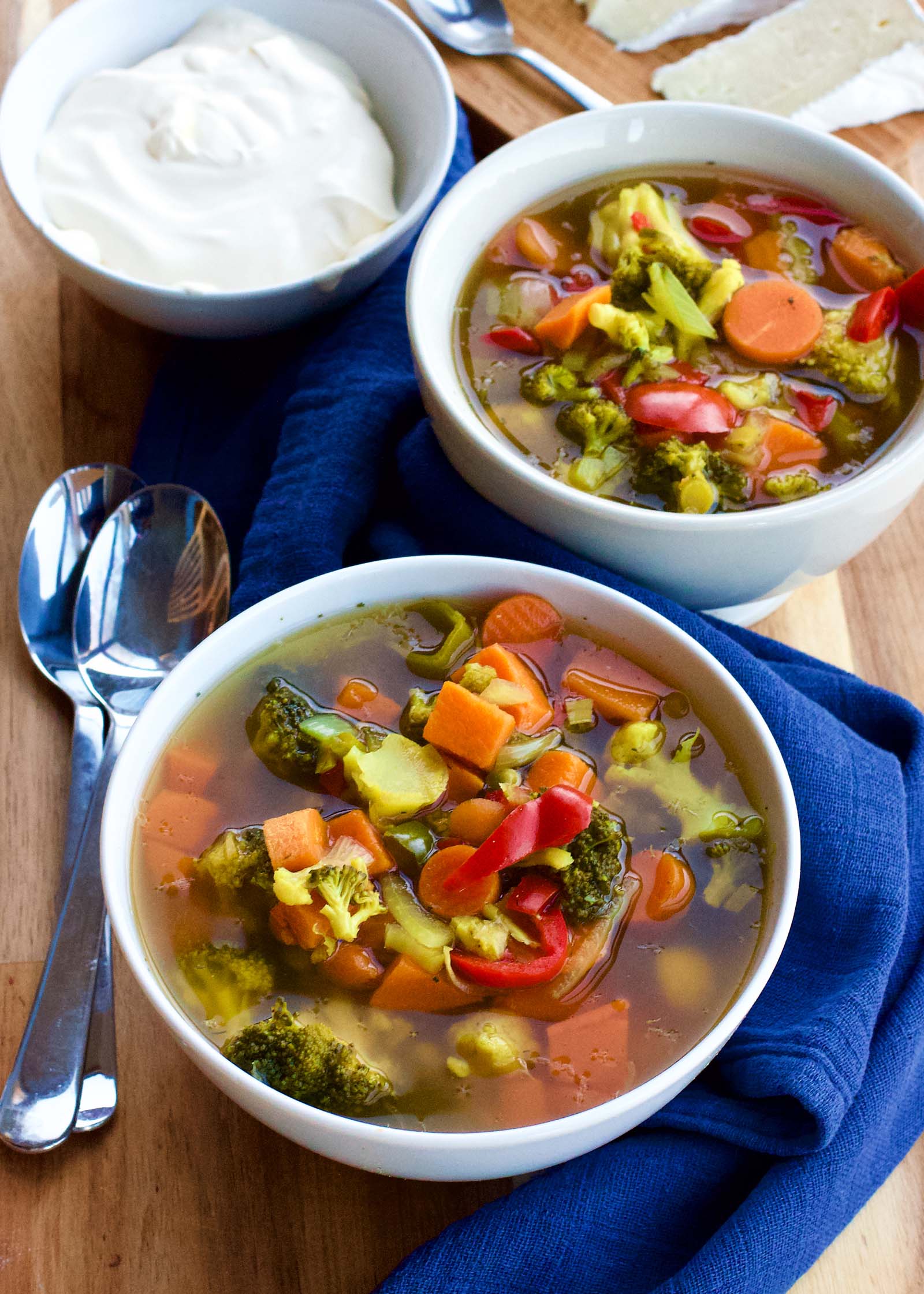 Two bowls of Spicy Colorful Vegetable Sour Soup on a table, brie cheese and sour cream on the side