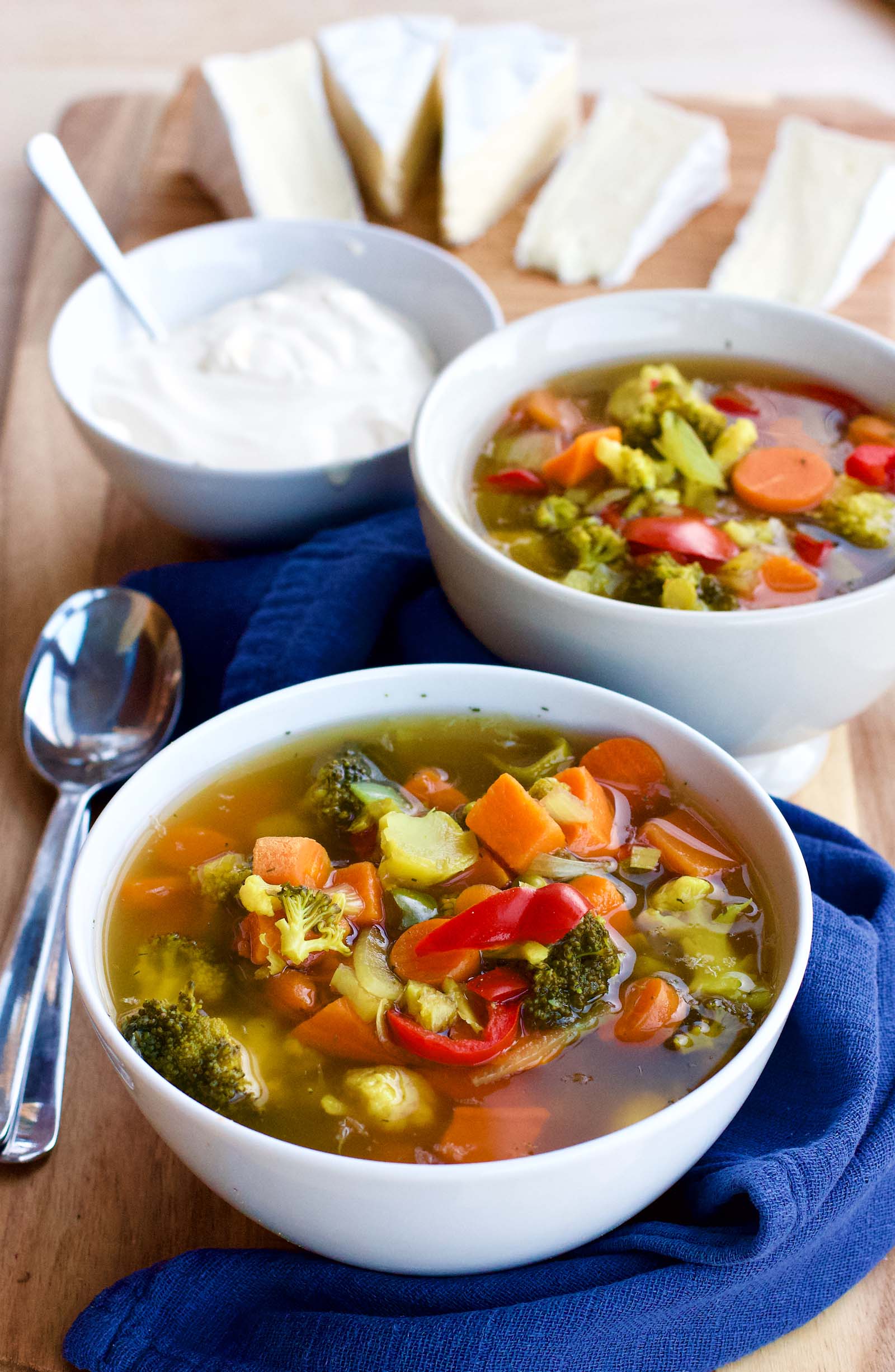 Two bowls of Spicy Colorful Vegetable Sour Soup on a table, served with brie cheese and full-fat sour cream