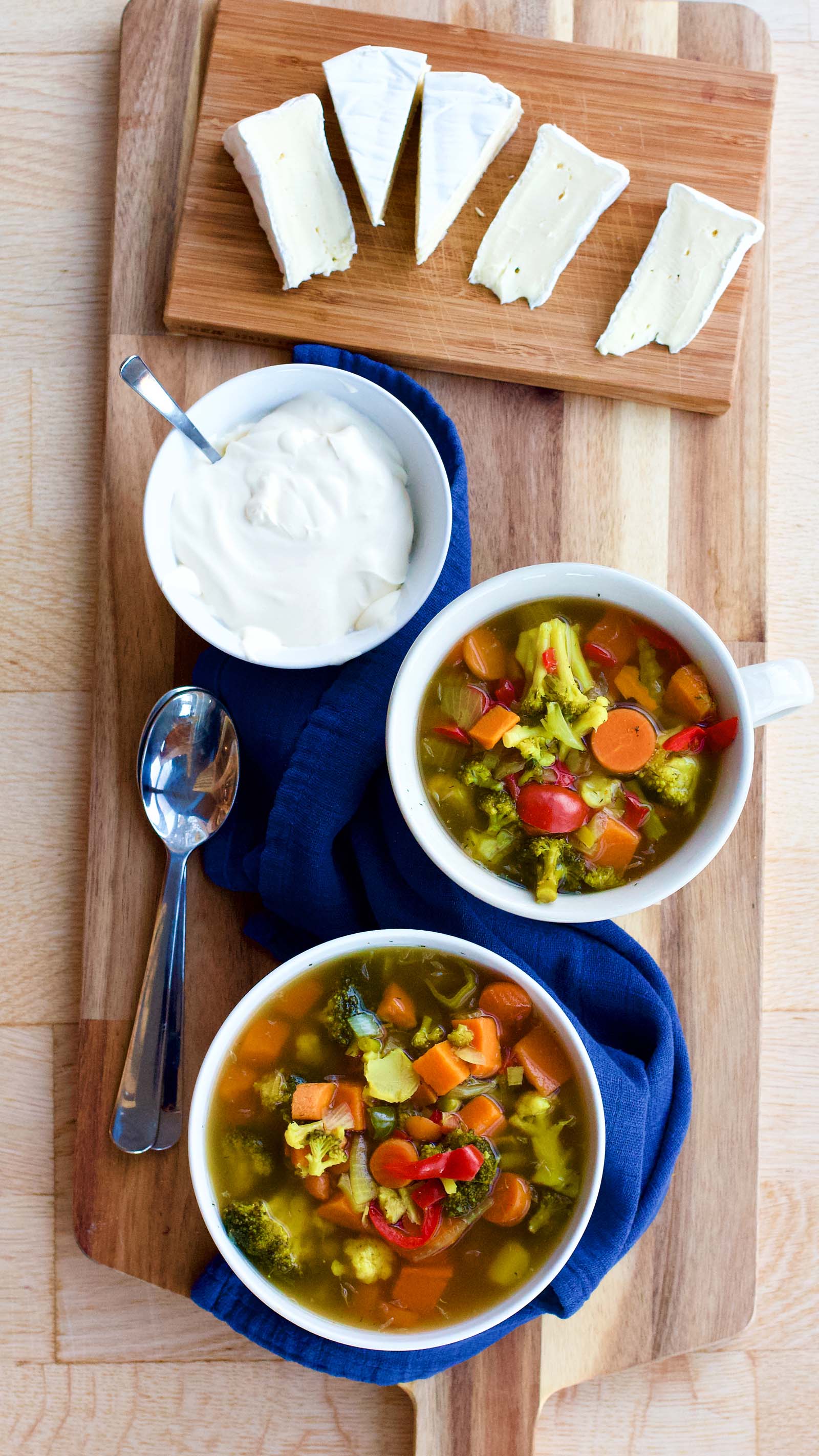 Top-down view with two bowls of Spicy Colorful Vegetable Sour Soup on a table, served with brie cheese and full-fat sour cream