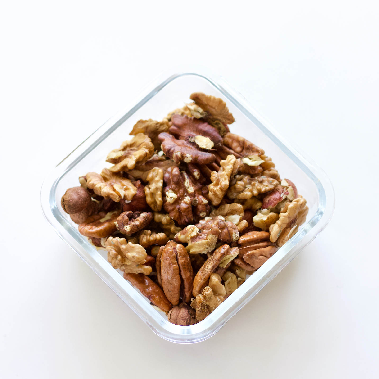 Walnuts, pecans and hazelnuts in a square-shaped glass tray, top-down view