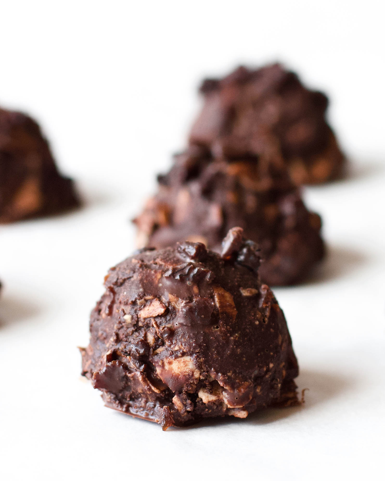 Close-up with one Chocolate Coconut Macaroon on a white backdrop, and other chocolate macaroons in the background