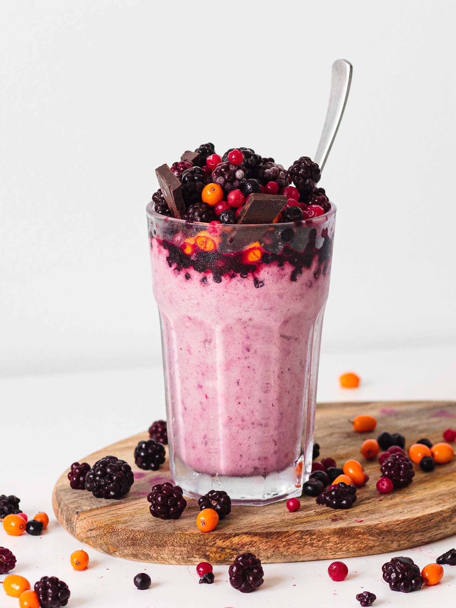 Glass with freshly made Keto Frozen Berry Milkshake on a white background and frozen berries all around