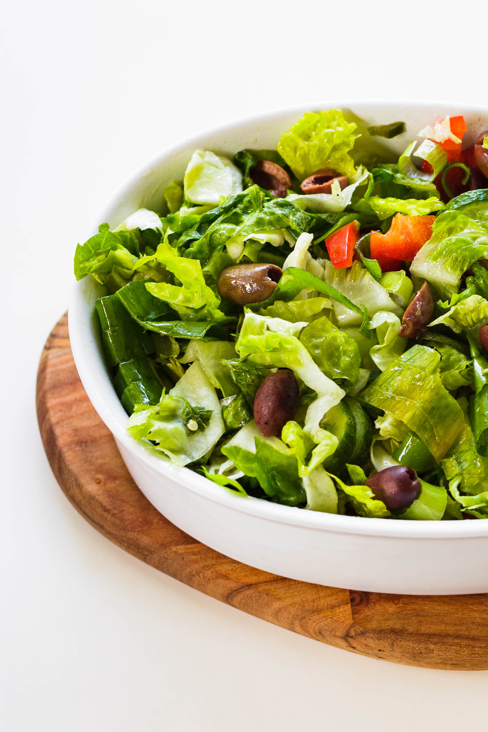 Close-up shot of white bowl with freshly made Simple Green Salad, left side