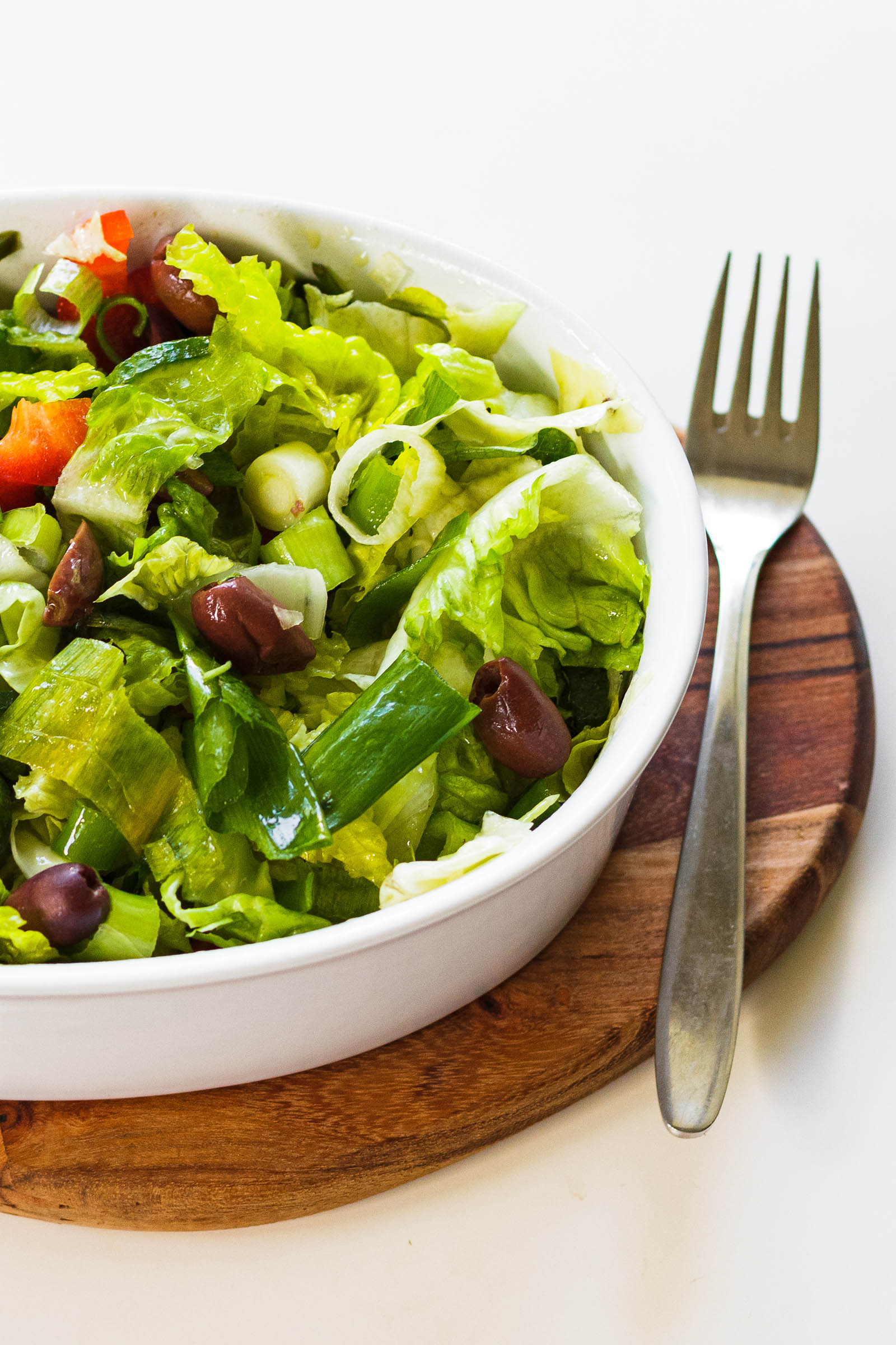 Close-up shot of white bowl with freshly made Simple Green Salad and fork, right side