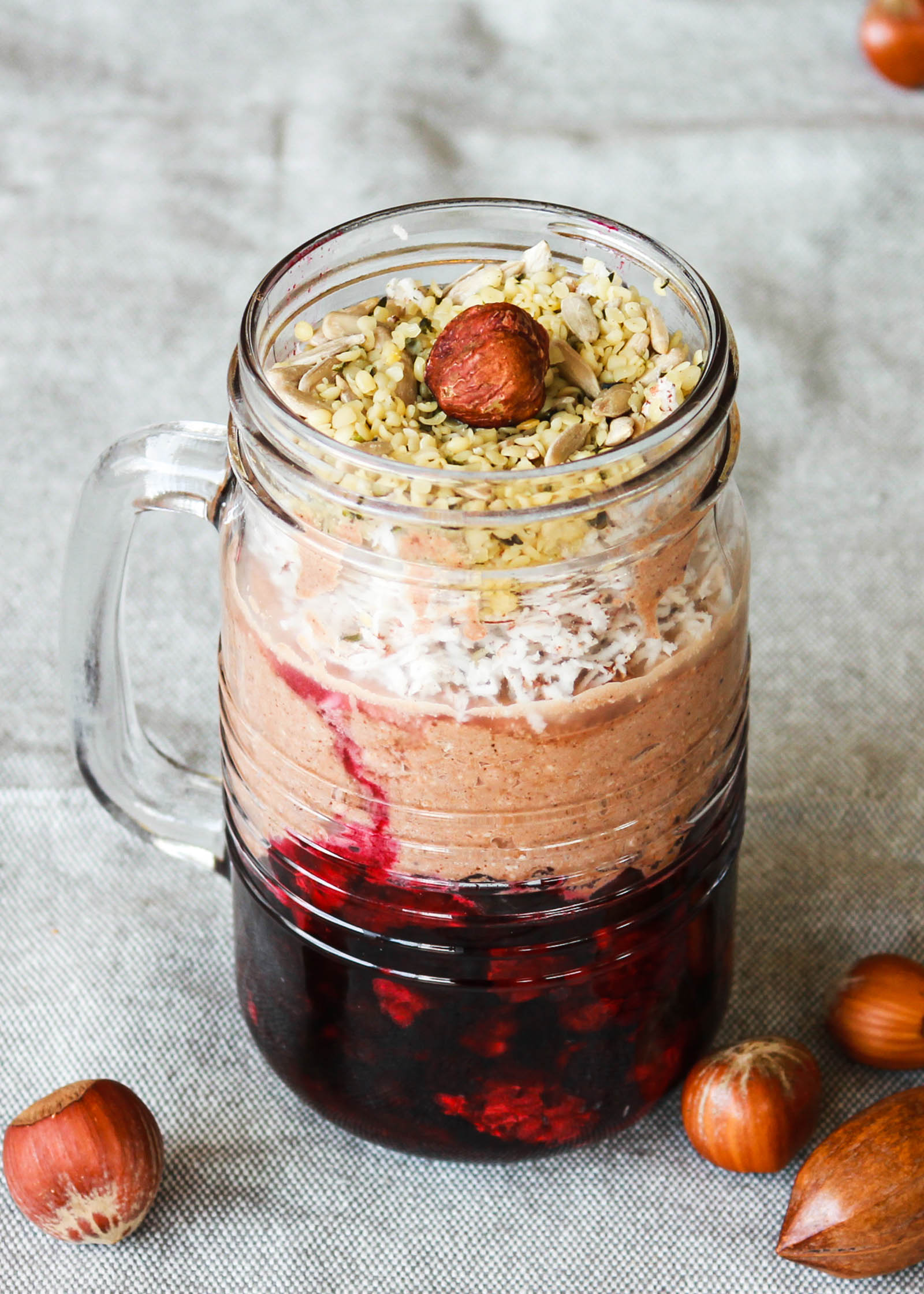 Mug with 3-Layer Raw Vegan Winter Dessert and hazelnuts on the side, close-up shot