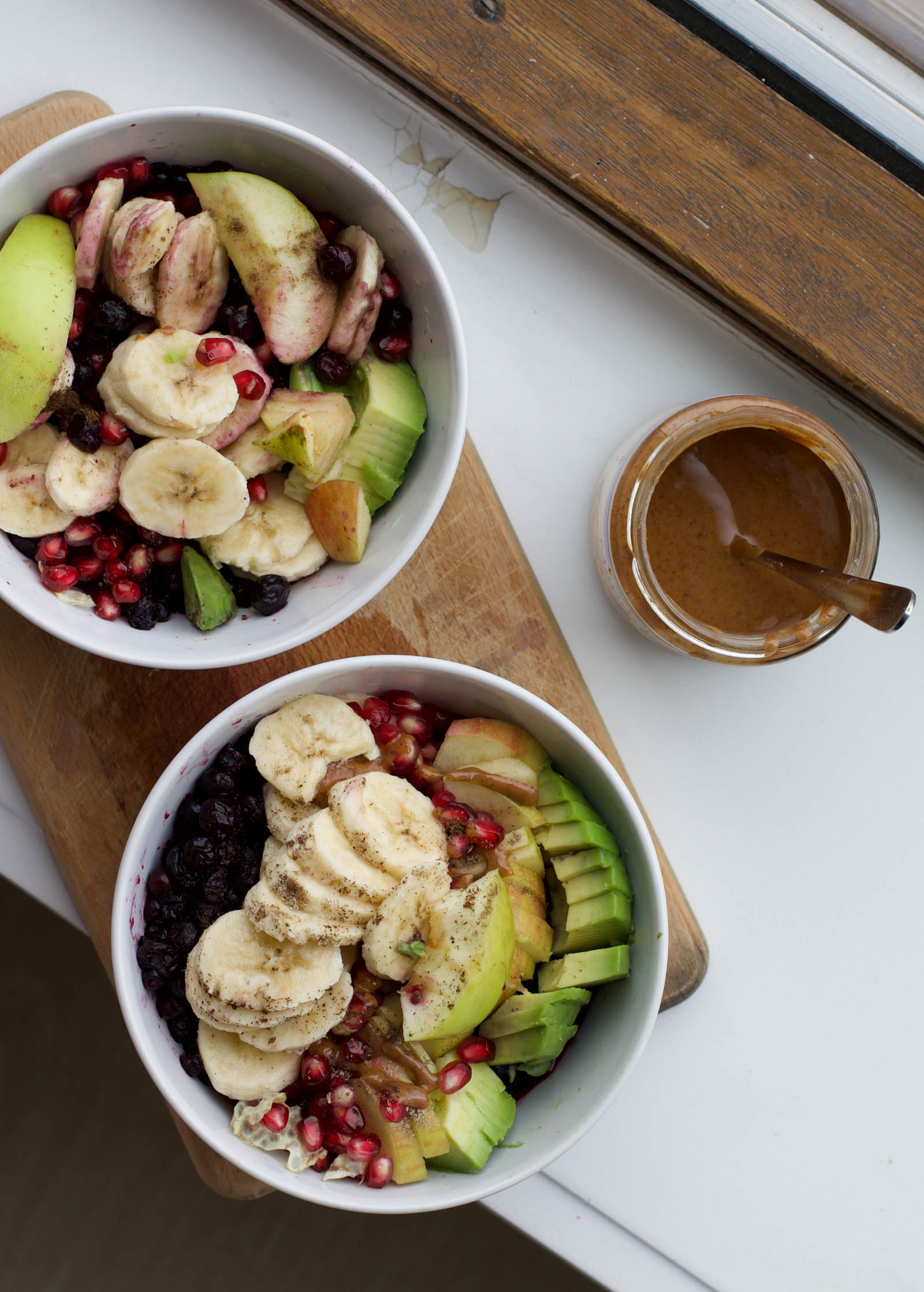 Two servings of freshly made Real-Deal Raw Fruit Bowl and jar of almond butter, top-down view