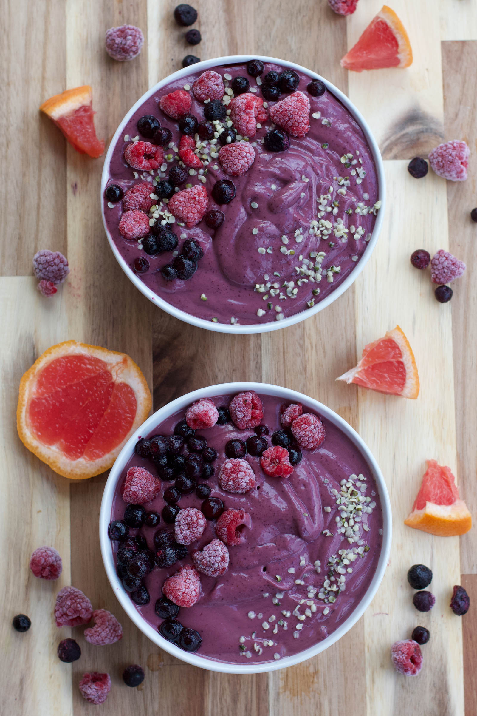 Two bowls of freshly made Purple Smoothie Bowl on a wooden table, top-down view