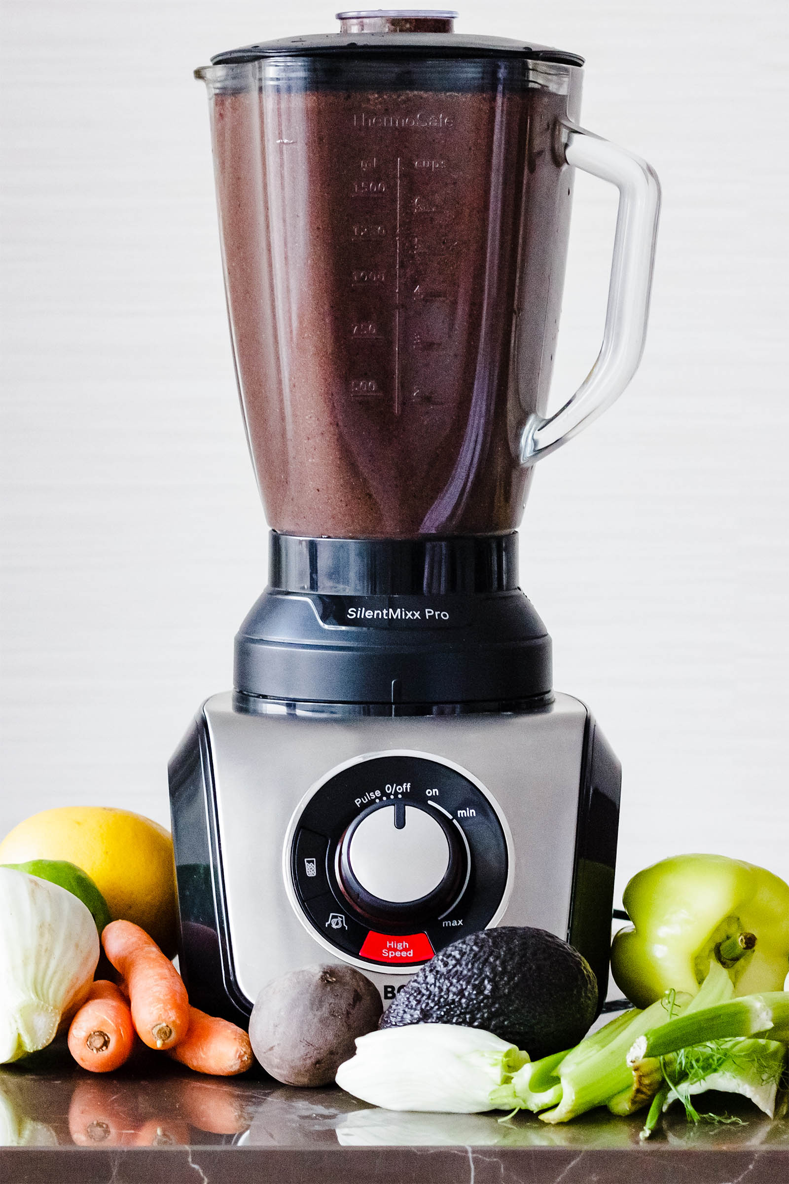 Big blender with freshly made Spinach Blueberry Beet Surprise Smoothie on a table, with different fruits and vegetables around