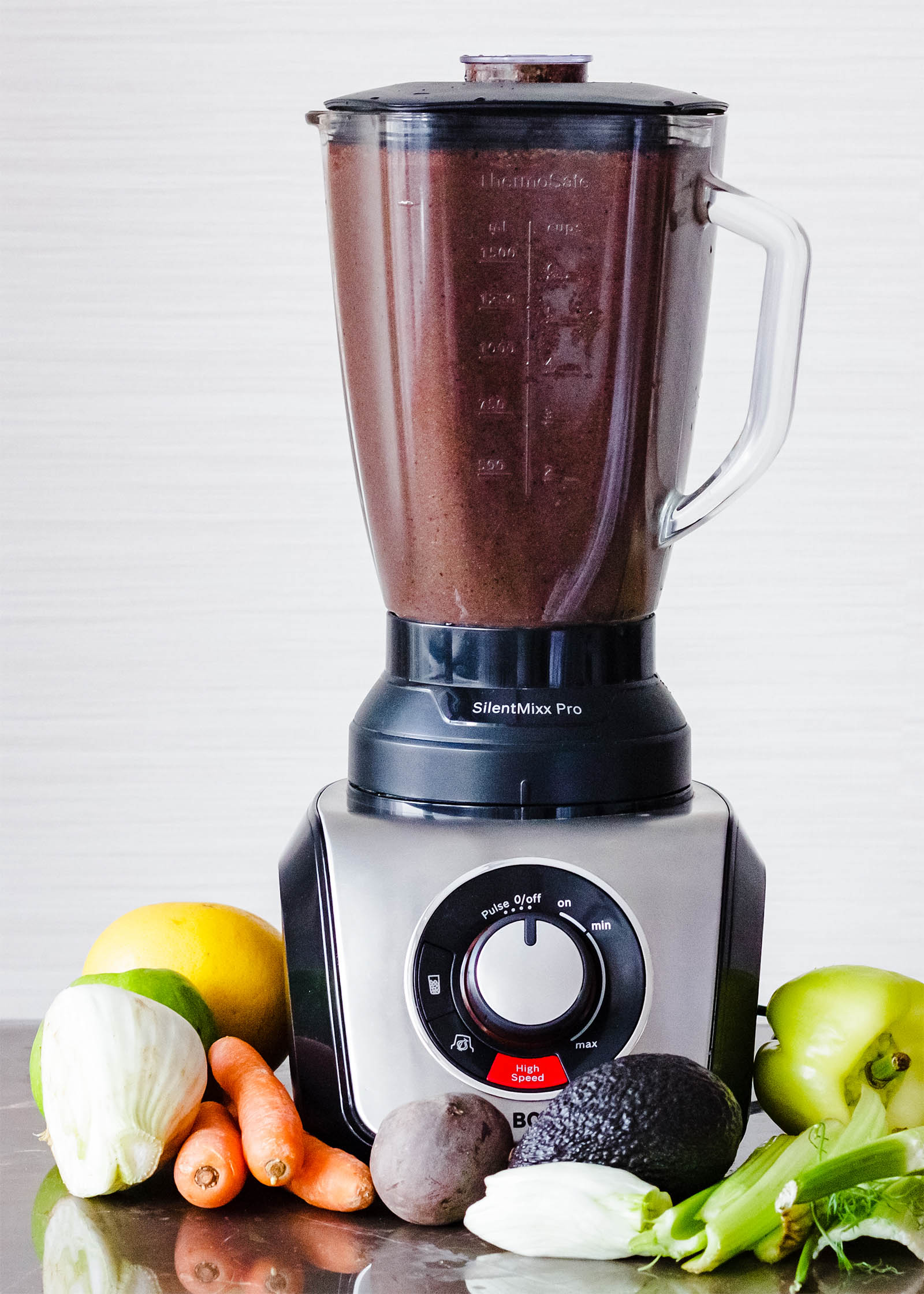 Big blender with freshly made Spinach Blueberry Beet Surprise Smoothie on a table, with different fruits and vegetables around