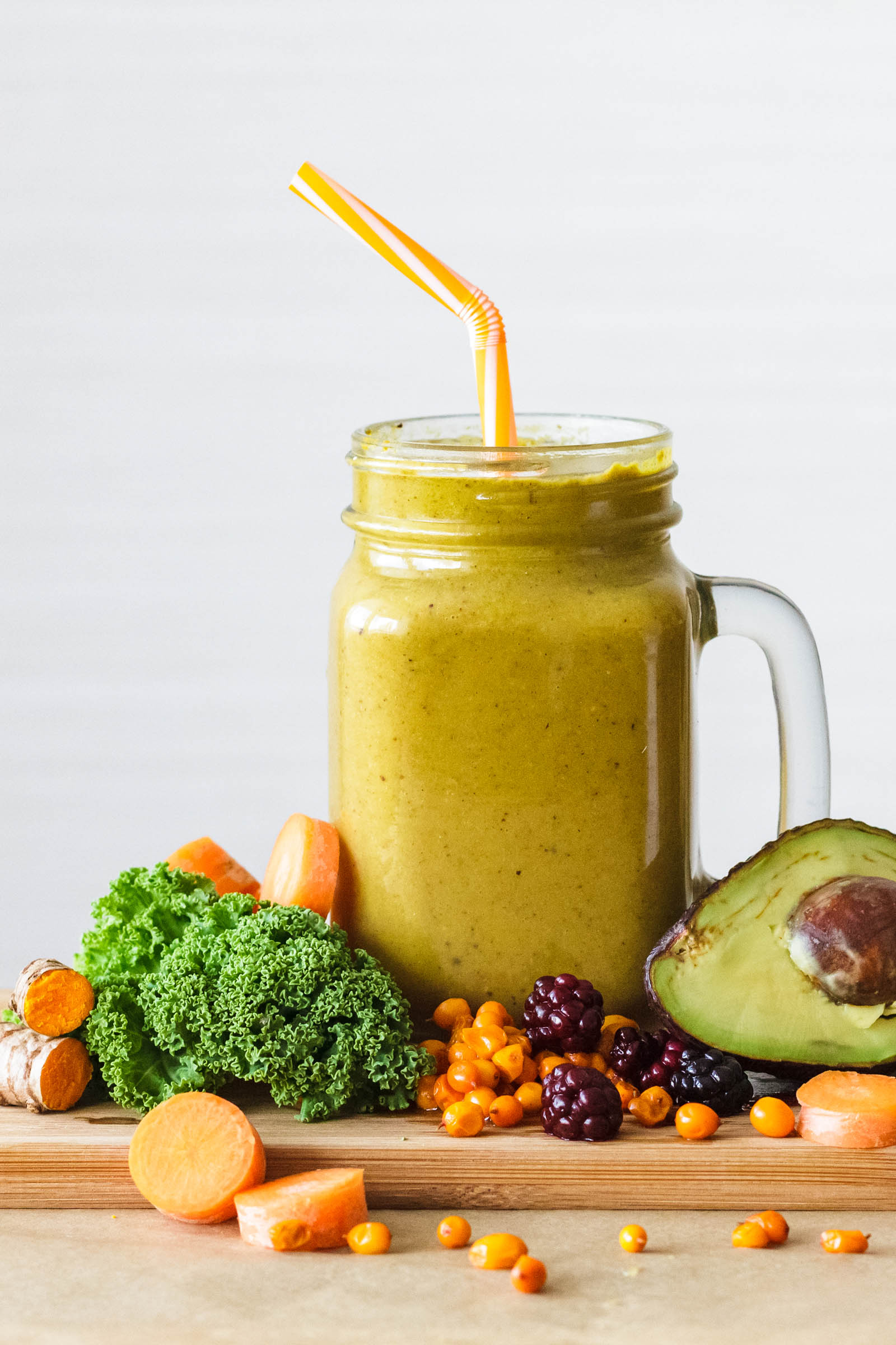 One jar of freshly made Yellow Superfood Smoothie with Avocado, Berries and Vegetable, and fresh plants around on a table