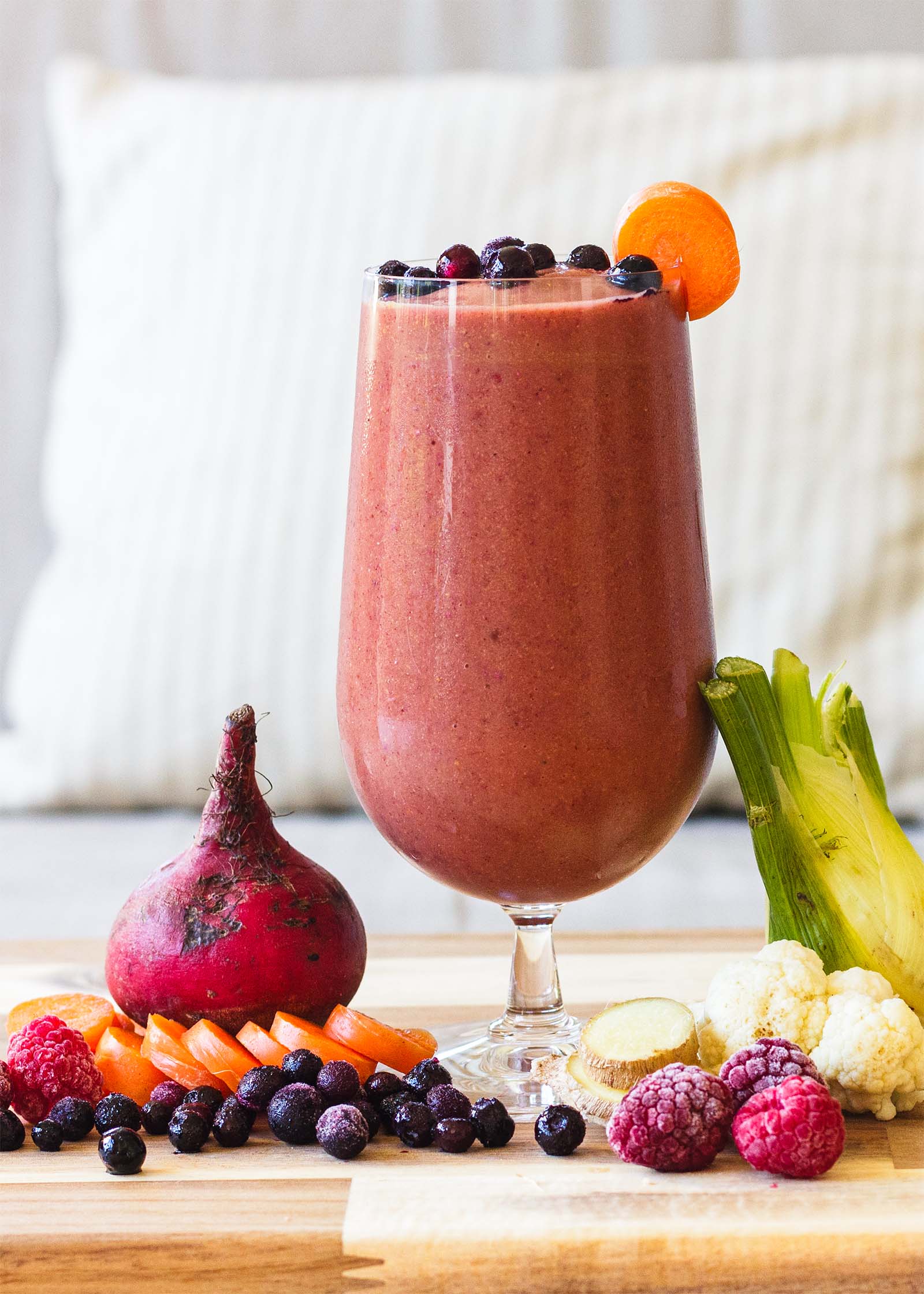 Glass with Beet Berry Cauliflower Refreshing Fall Smoothie on a table, and fresh plants around