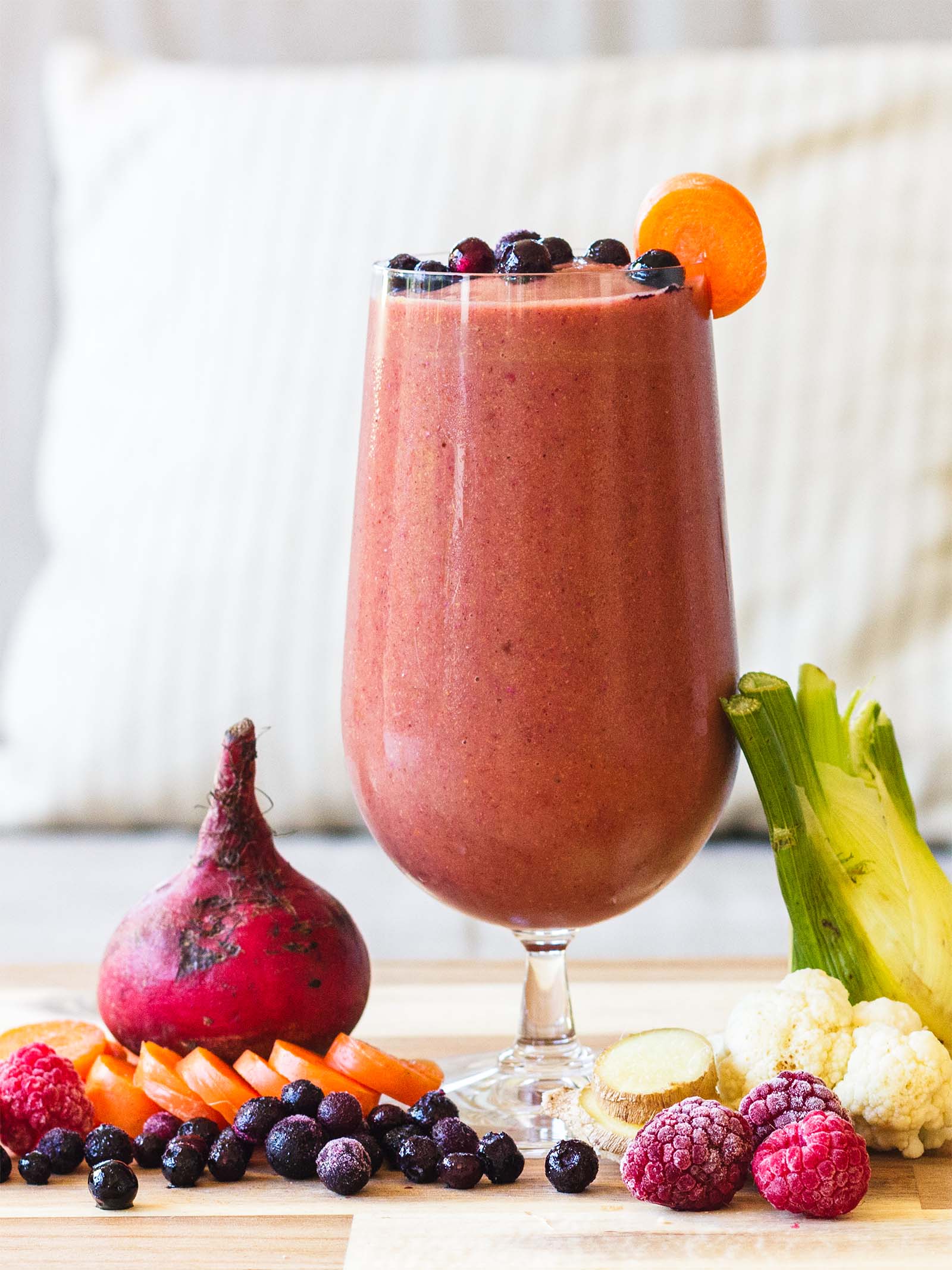 Glass with Beet Berry Cauliflower Refreshing Fall Smoothie on a table, and fresh plants around